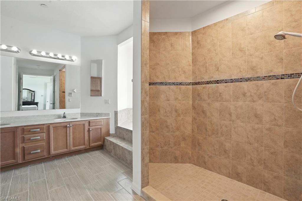 Spacious bathroom featuring a dual vanity with light-colored countertops, wood cabinetry, and a large mirror