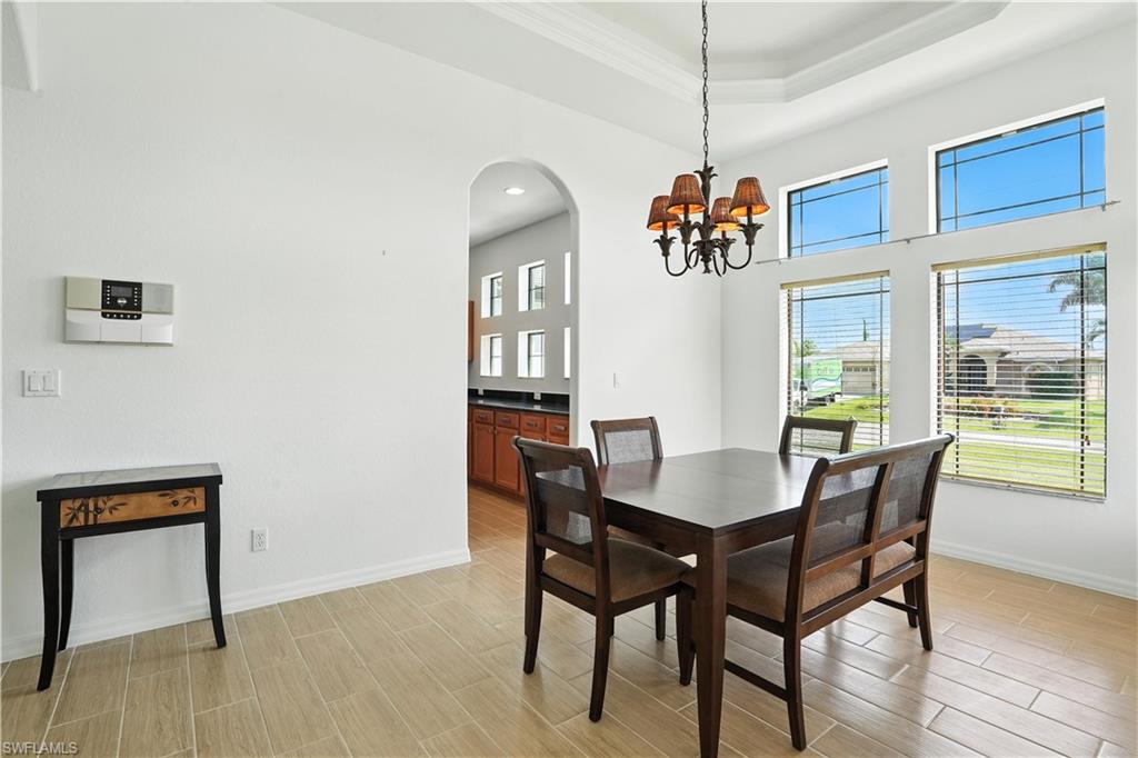 Dining area featuring high tray ceilings, a chandelier with decorative shades, large windows with horizontal blinds, and tile flooring