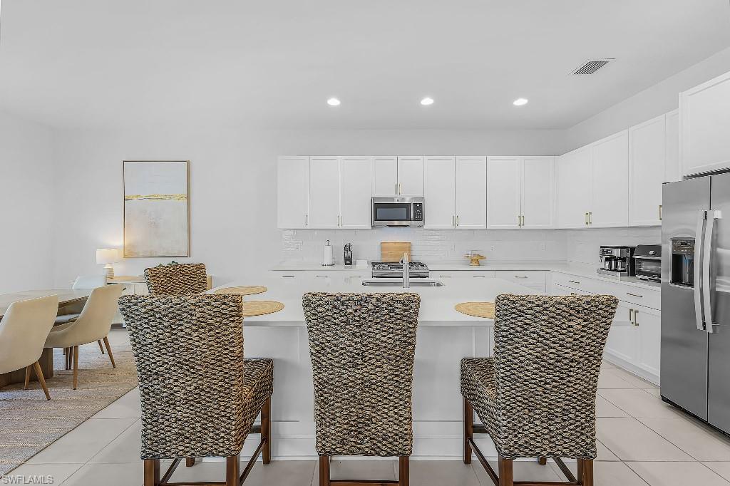 Kitchen featuring white shaker cabinetry, stainless steel appliances, a center island with sink, and a tile backsplash