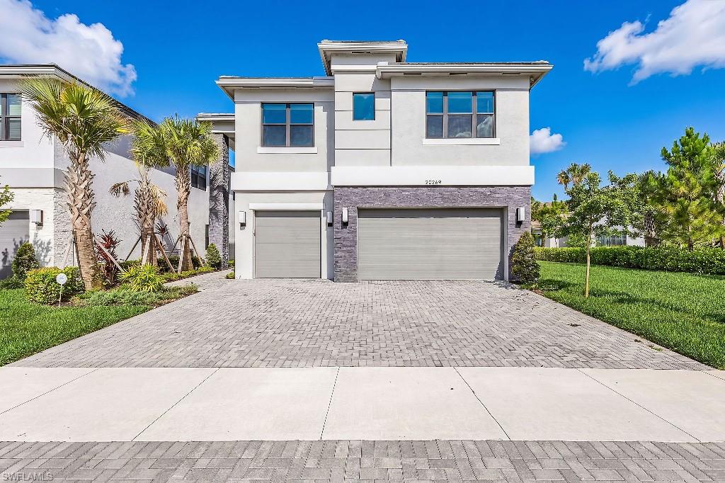 Modern architectural facade featuring stacked stone accents, dual garage doors, and a paver driveway