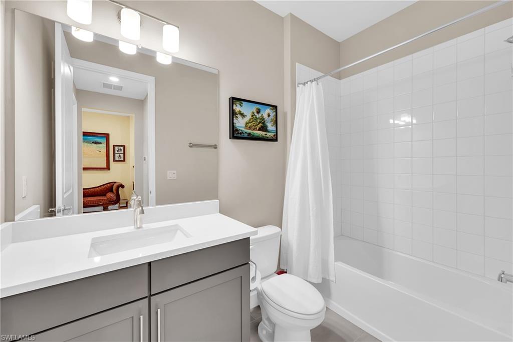 Bathroom featuring a white rectangular undermount sink, a gray vanity with double-door cabinetry, a white countertop, and a built-in bathtub with white subway tile surround