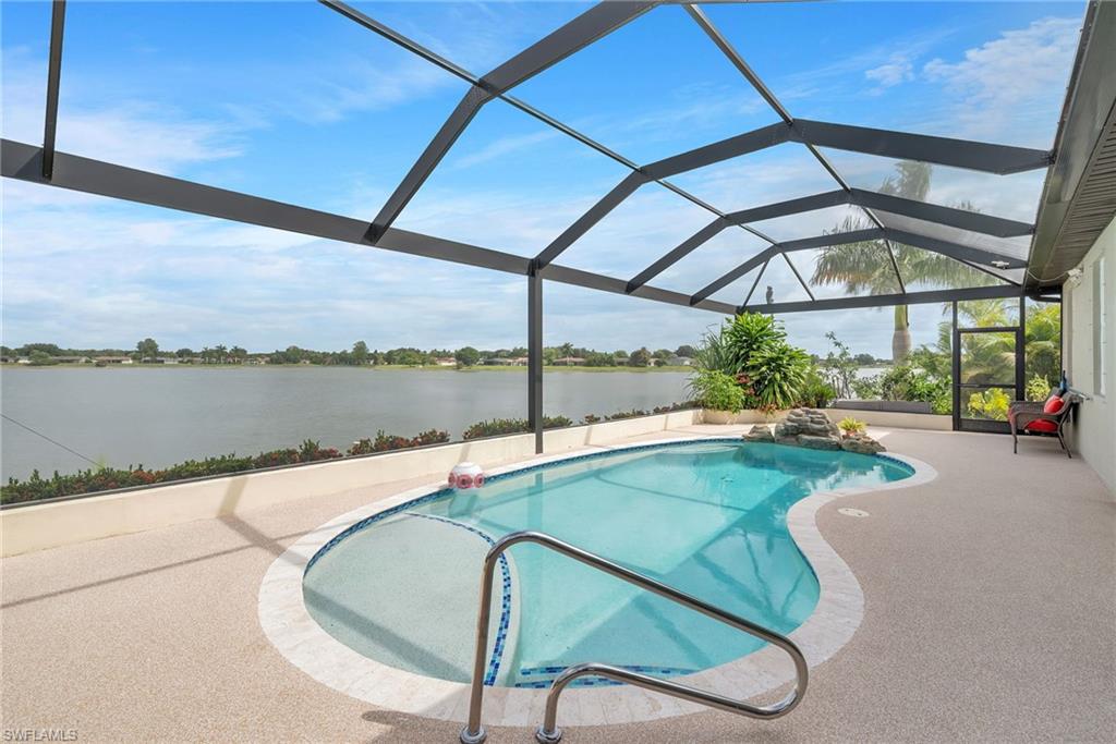 Screened-in pool deck featuring a freeform pool with integrated waterfall feature, water frontage, and surrounding tropical landscaping