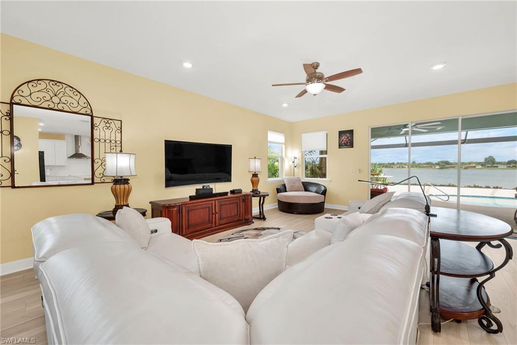 Spacious living area featuring large sliding glass doors, light wood-finish flooring, a ceiling fan with integrated lighting, recessed lighting, and expansive water views