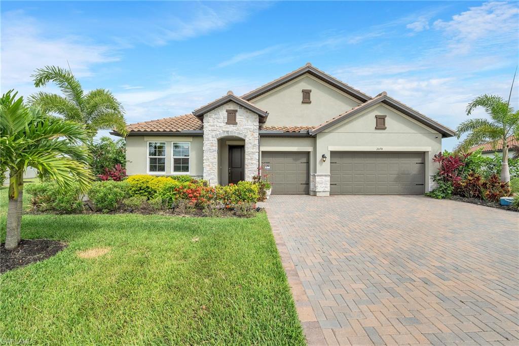 Stucco exterior with stone veneer accents, dual garage doors, a tile roof, and a paver driveway