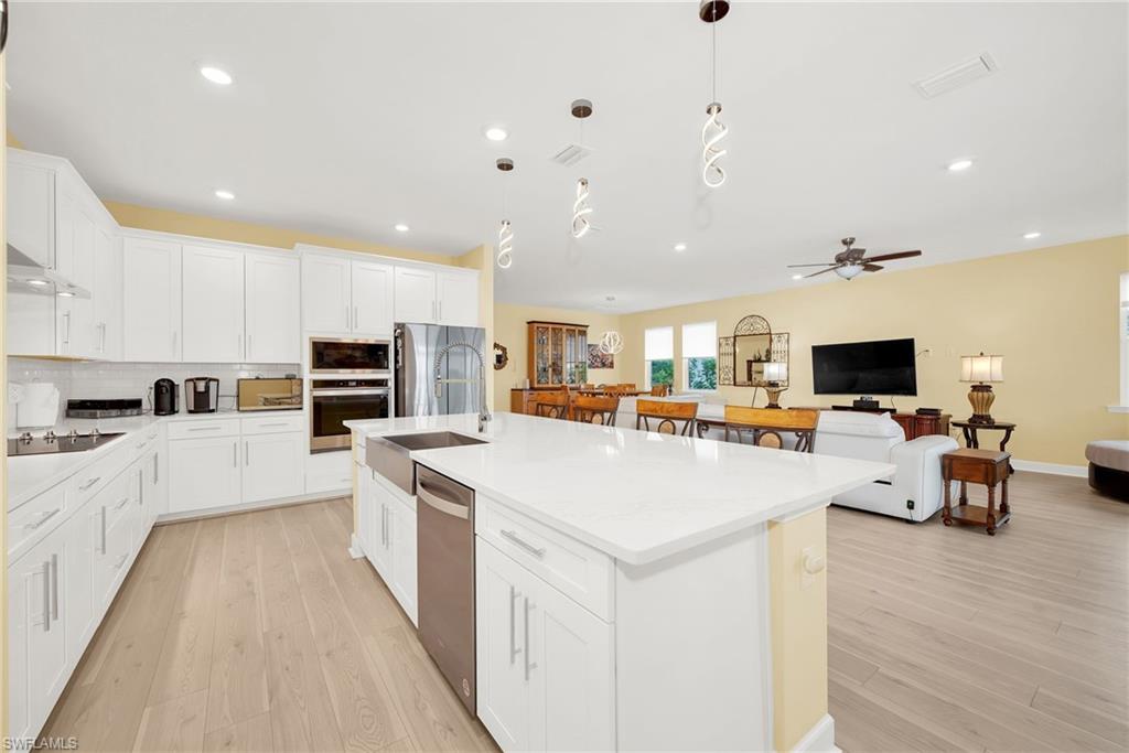 Open concept kitchen featuring an expansive island with a farmhouse sink, white shaker cabinetry, stainless steel appliances, and light wood-finish flooring