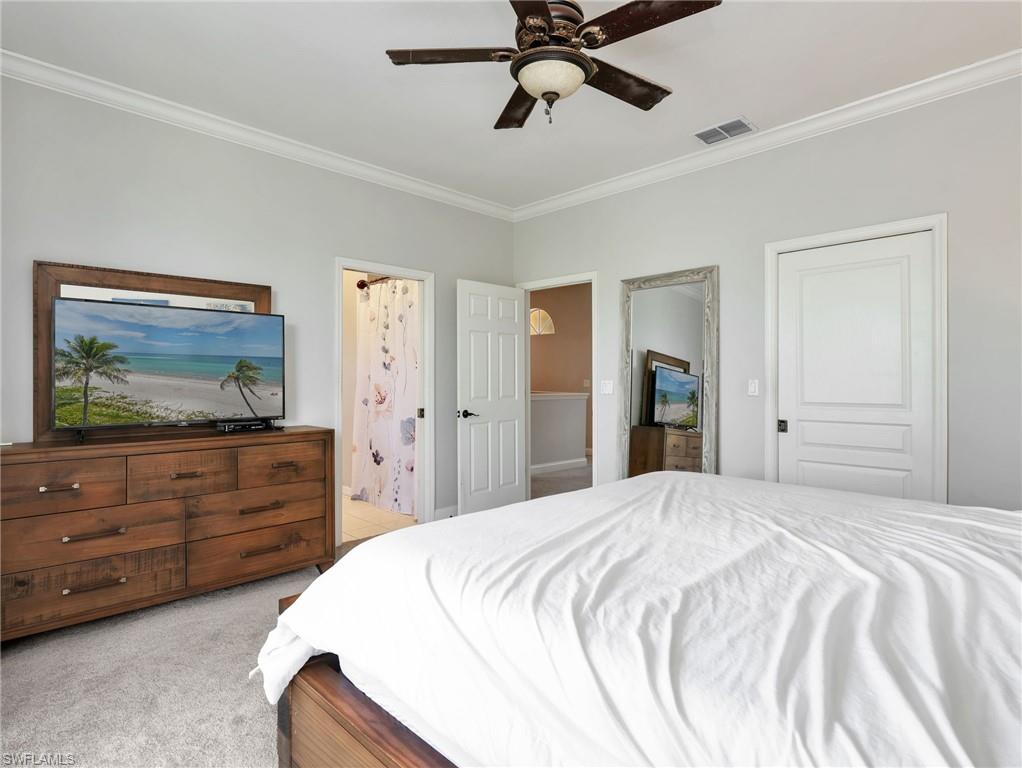 Carpeted interior room featuring crown molding, a dark wood-finish ceiling fan with integrated lighting, and white interior doors