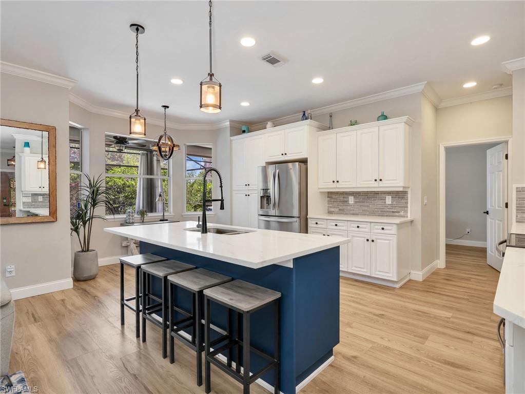 Open-concept kitchen featuring a spacious island with a white countertop and blue base, stainless steel appliances, white cabinetry with dark hardware, a tile backsplash, and wood-finish flooring
