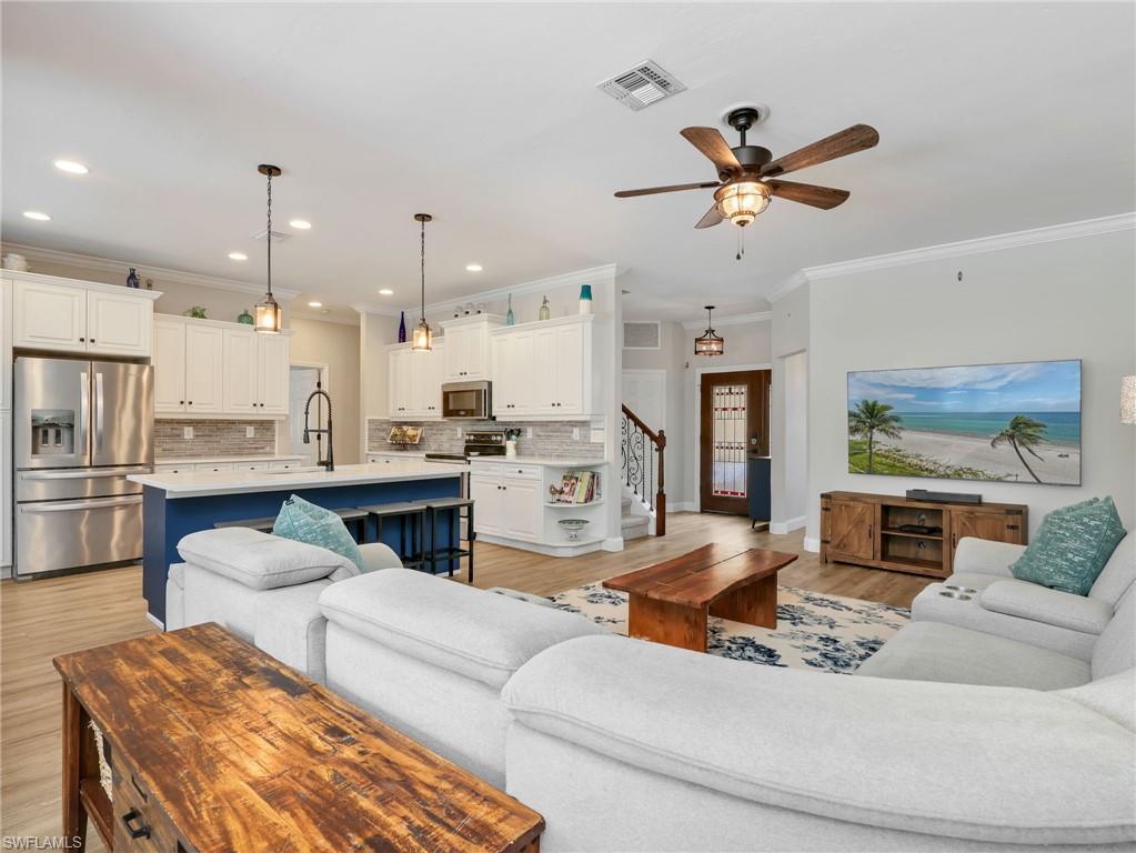 Open-concept living area featuring a kitchen with white cabinetry, stainless steel appliances, a blue island with seating, and pendant lighting
