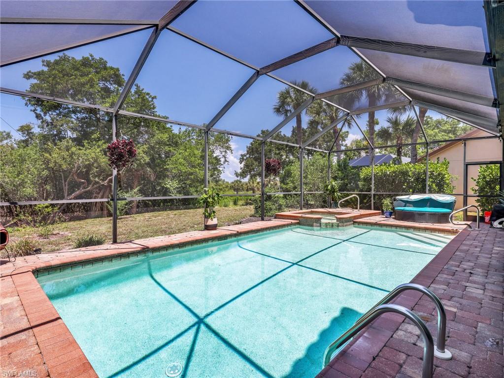 Screened pool enclosure featuring a rectangular swimming pool, integrated spa, and brick paver decking
