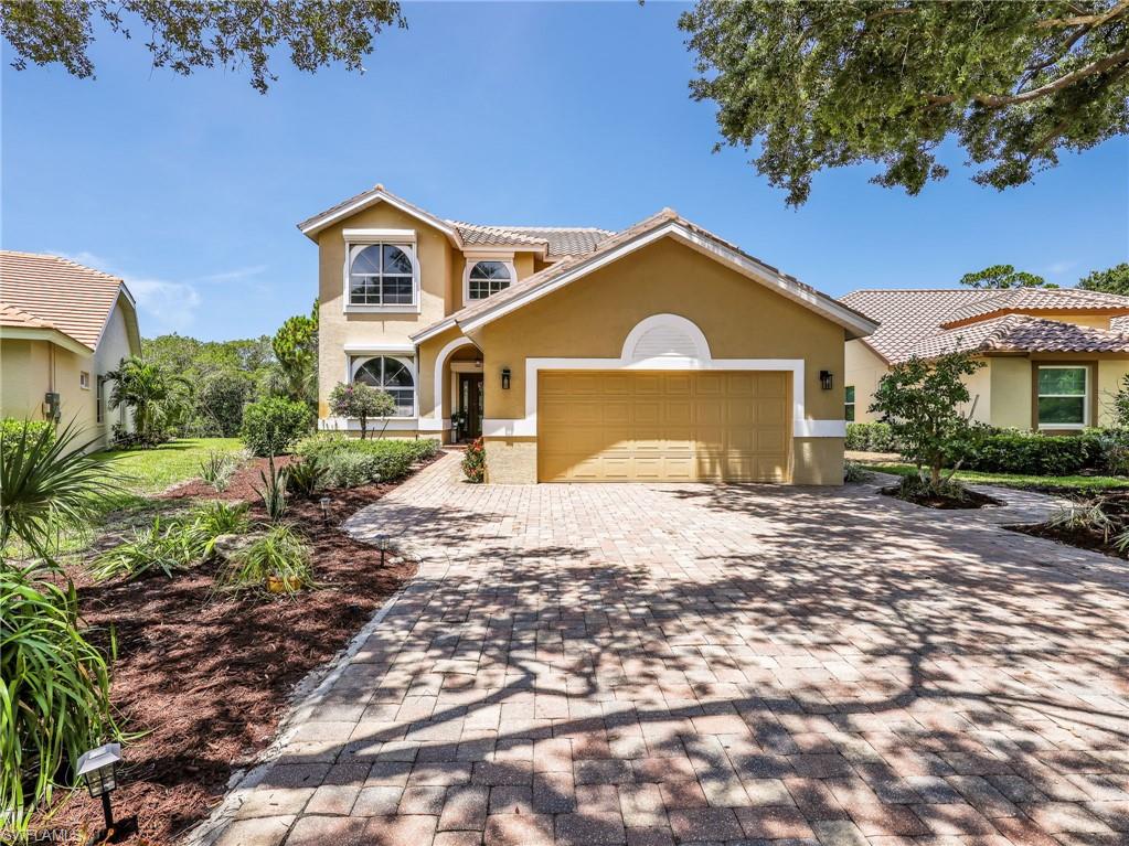 Stucco exterior with a tiled roof, paver driveway, arched entryway, and landscaped garden beds
