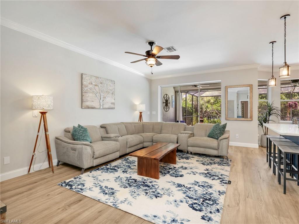 Spacious living area featuring wood-finish flooring, a ceiling fan, and crown molding