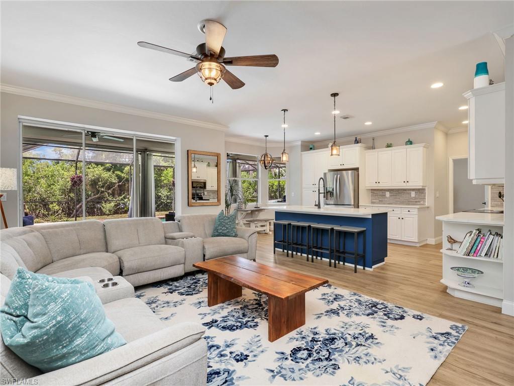 Open-concept living area featuring wood-finish flooring, a contemporary kitchen island with seating, white shaker cabinetry, stainless steel appliances, and large sliding glass doors opening to the exterior