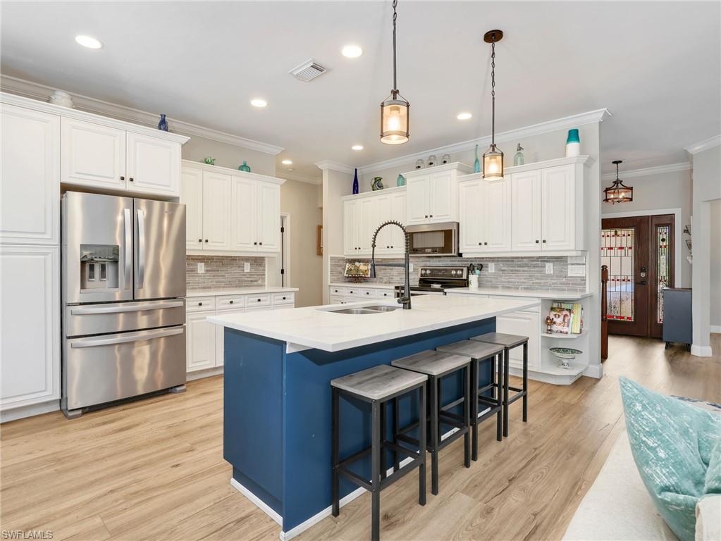 Kitchen featuring a blue-toned island with seating, pendant lighting, white cabinetry, stainless steel appliances, and wood-finish flooring