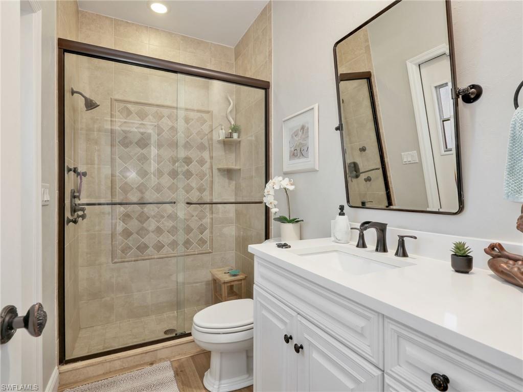 Bathroom featuring a tiled shower with glass enclosure, white vanity with integrated sink, black fixtures, and wood-finish flooring