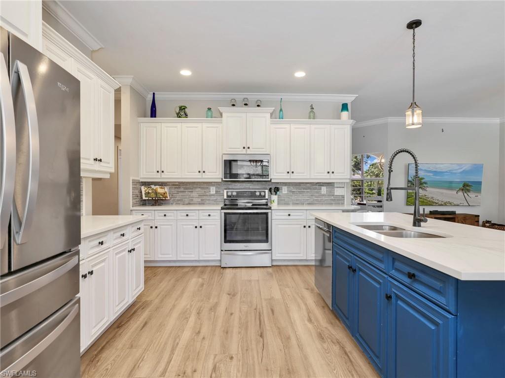 Spacious kitchen featuring white cabinetry, stainless steel appliances, a light-toned backsplash, and a contrasting blue island with a double sink