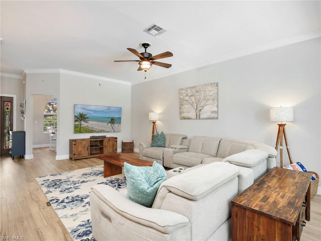 Living area featuring light wood-finish flooring, white crown molding, a ceiling fan with light fixture, and an arched entry