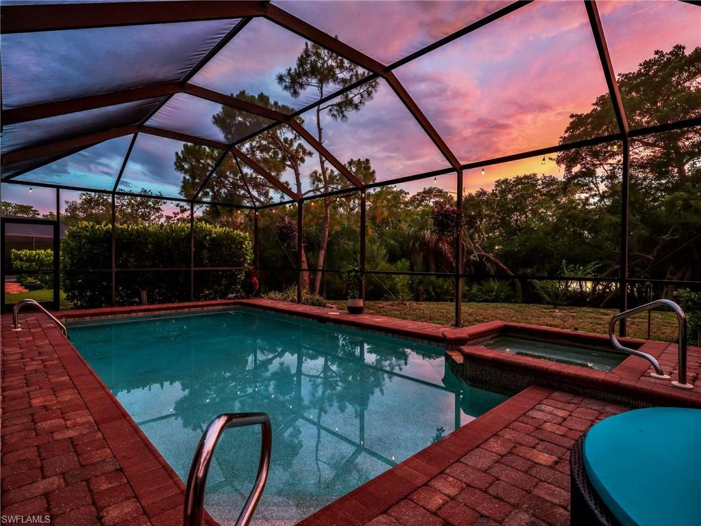 Screened enclosure featuring a swimming pool, integrated spa, and red brick paver deck