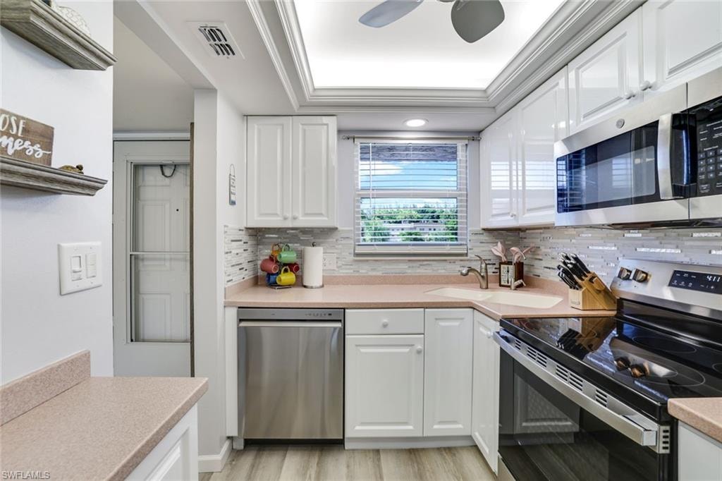 Kitchen with appliances with stainless steel finishes, white cabinets, a tray ceiling, tasteful backsplash, and crown molding