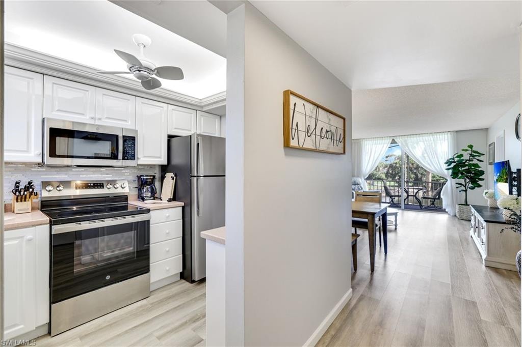 Kitchen featuring stainless steel appliances, white cabinets, light wood-style flooring, ceiling fan, and decorative backsplash