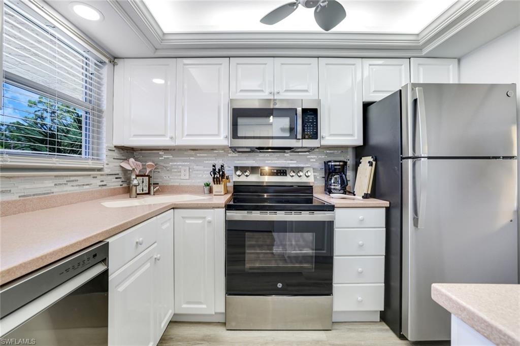 Kitchen with appliances with stainless steel finishes, white cabinets, decorative backsplash, crown molding, and a tray ceiling