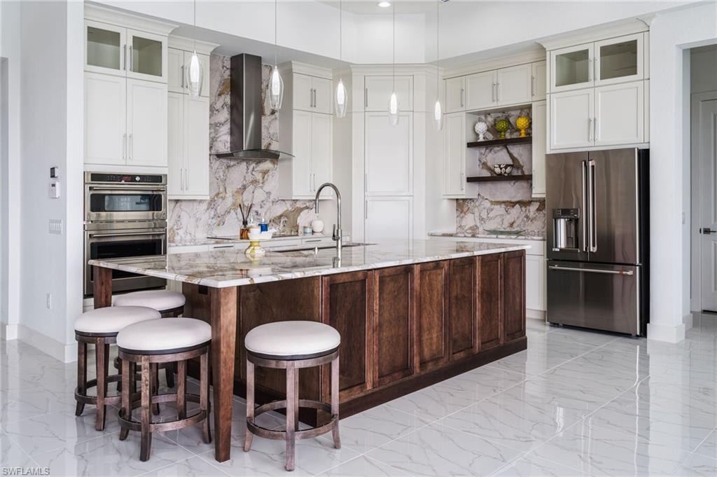 Spacious kitchen featuring an expansive center island with seating, stainless steel appliances, white upper cabinetry, and a granite backsplash