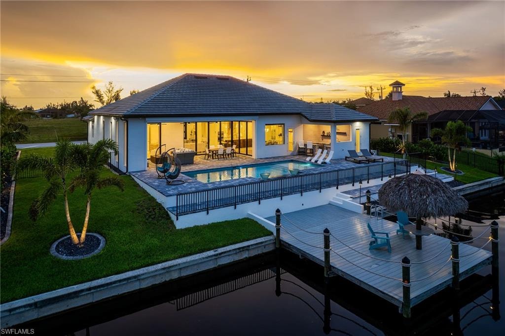 Waterfront residence featuring a spacious patio, private swimming pool, expansive sliding glass doors, a manicured lawn, and a private dock