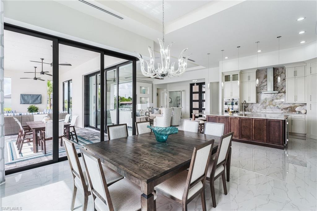 Spacious interior featuring large format tile flooring, a clear glass chandelier, and an open concept kitchen with light-toned cabinetry, a large center island, and a granite backsplash with a range hood