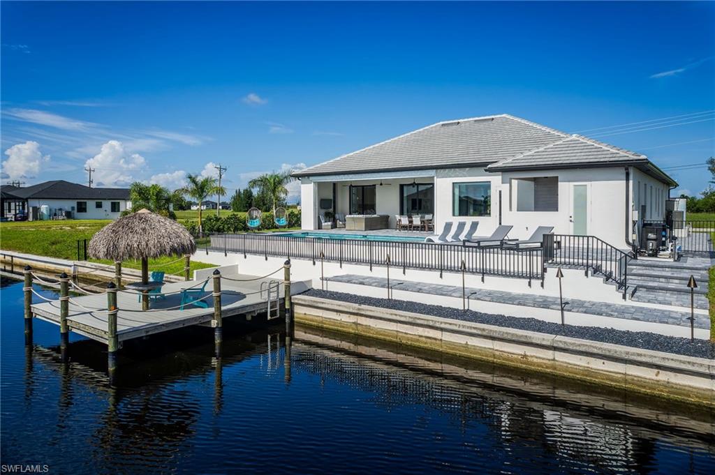 Waterfront property featuring a private dock with tiki hut, an in-ground swimming pool, and an expansive paved patio area