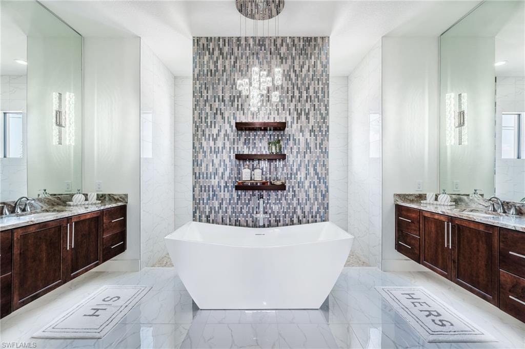 Primary bathroom with freestanding soaking tub with a mosaic tile accent wall and custom shelving