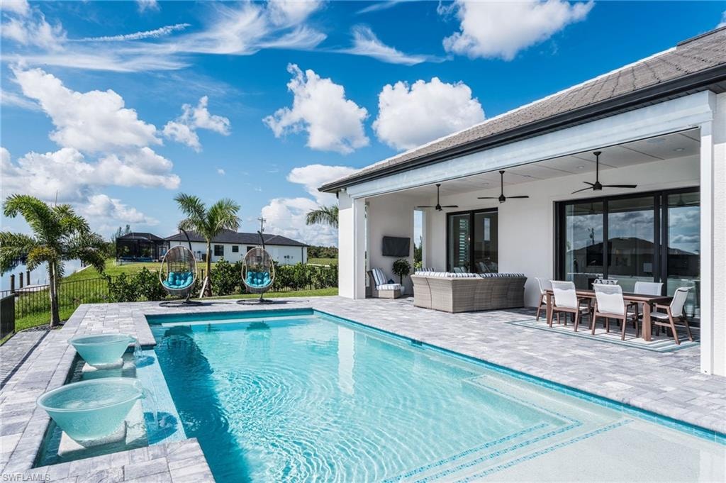 Expansive outdoor living area featuring a rectangular swimming pool with integrated water features, a paver patio, a covered lanai with ceiling fans, and sliding glass doors
