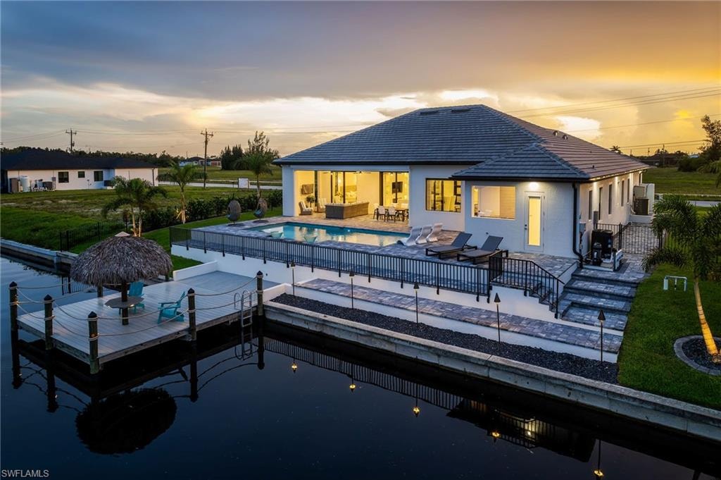 Waterfront property featuring a private boat dock with a thatched-roof tiki hut, a swimming pool, and a spacious paver patio