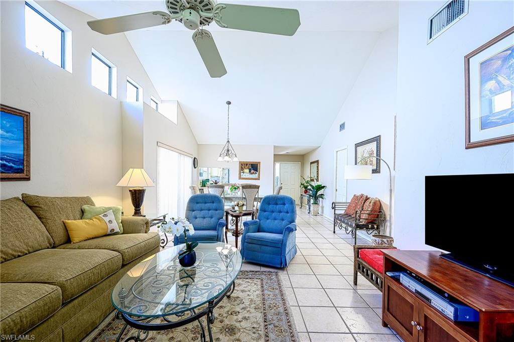 Tiled living room with high vaulted ceiling and ceiling fan with notable chandelier