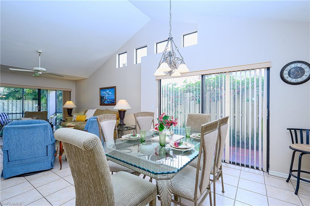 Dining room with light tile patterned floors, ceiling fan with notable chandelier, and high vaulted ceiling