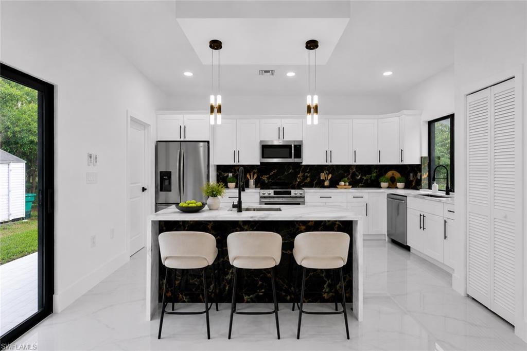 Modern kitchen featuring white cabinetry, stainless steel appliances, a black and white marble-look backsplash, and a large island with a quartz countertop