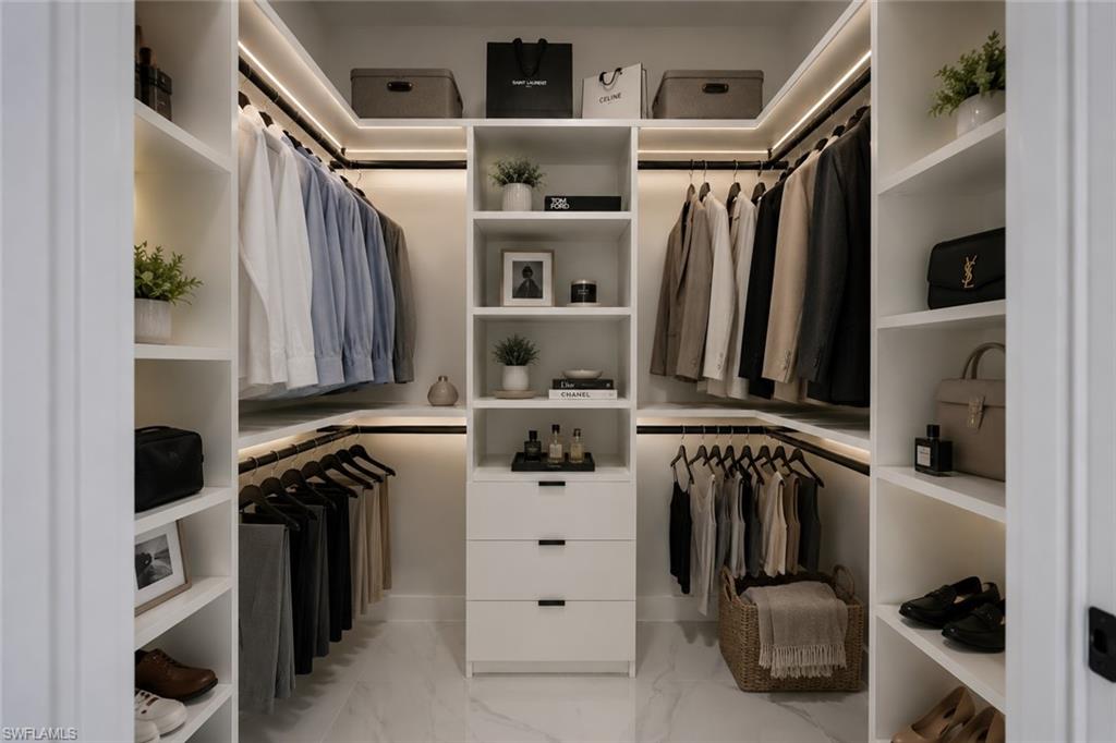 Walk-in closet featuring custom white cabinetry, integrated LED lighting, multiple hanging rods, open shelving, and a central dresser with three drawers