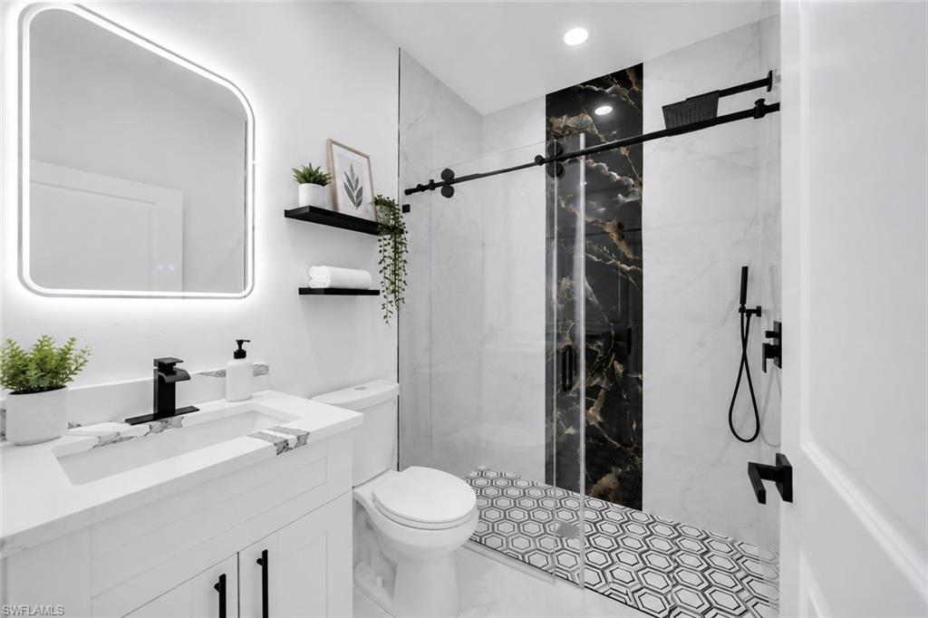 Bathroom featuring a white vanity with a stone-finish countertop, black faucet, and an illuminated mirror