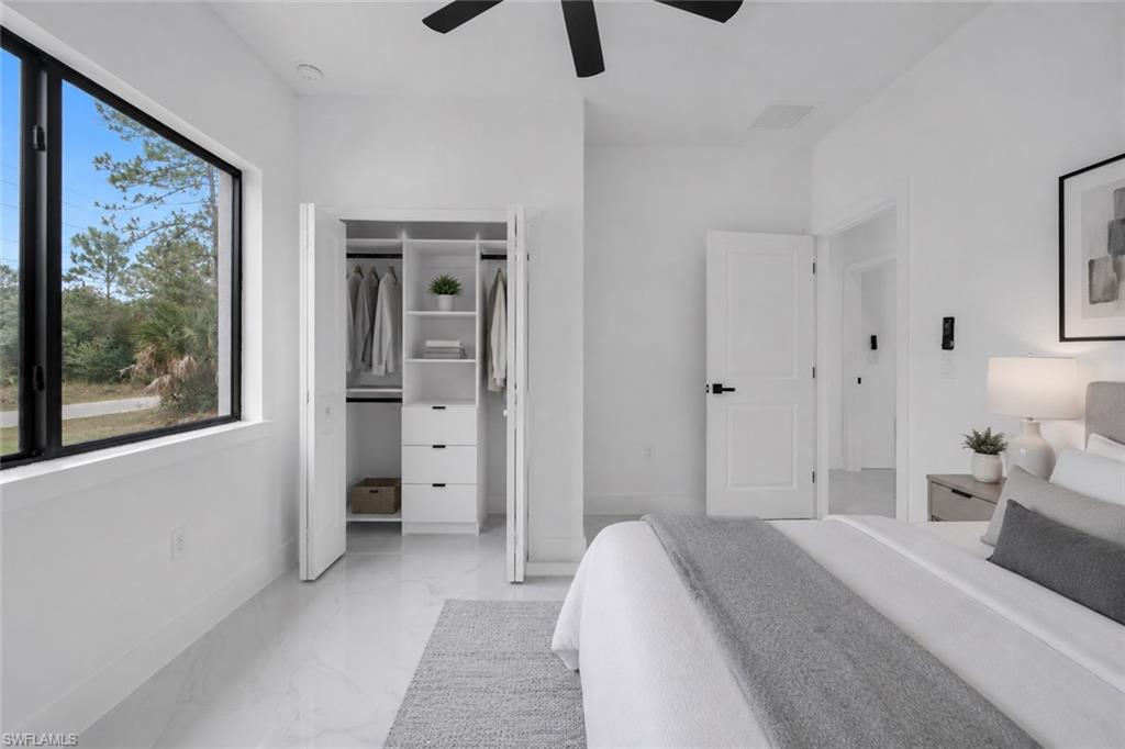 Bedroom featuring a large rectangular window with black trim, a built-in closet system with drawers and shelving, white walls, and light-colored tile flooring