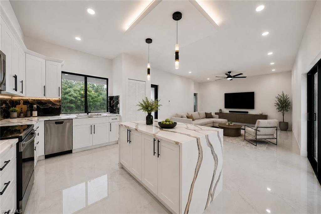 Open-concept interior featuring a gourmet kitchen with a waterfall island, white cabinetry, integrated stainless steel appliances, and dark veined backsplash