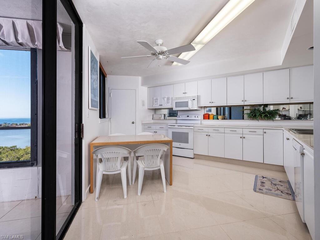 Kitchen featuring white cabinets, a kitchen bar, light tile patterned floors, ceiling fan, and white appliances
