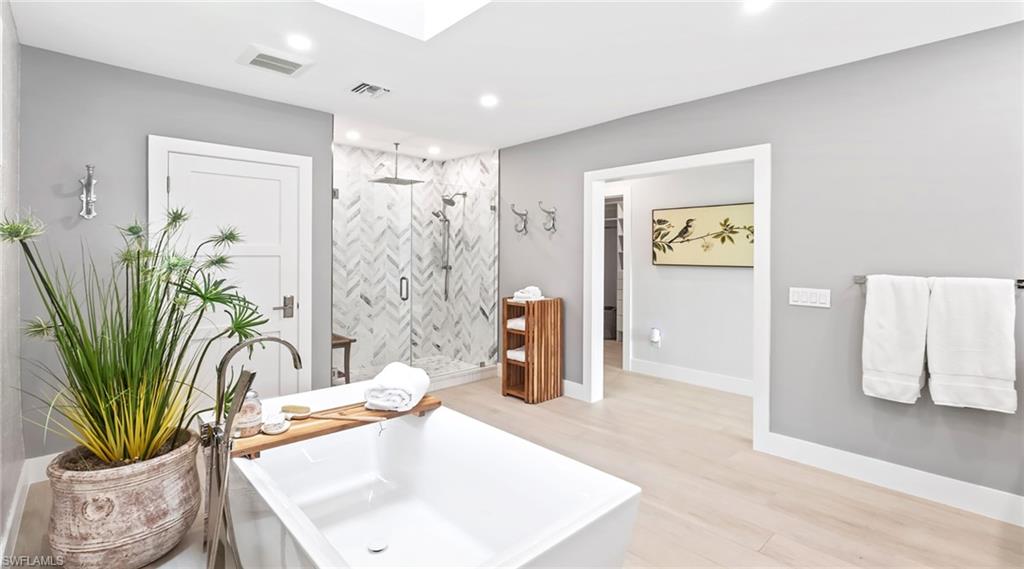 Bathroom with a stall shower, light wood-style flooring, a freestanding tub, recessed lighting, and a skylight