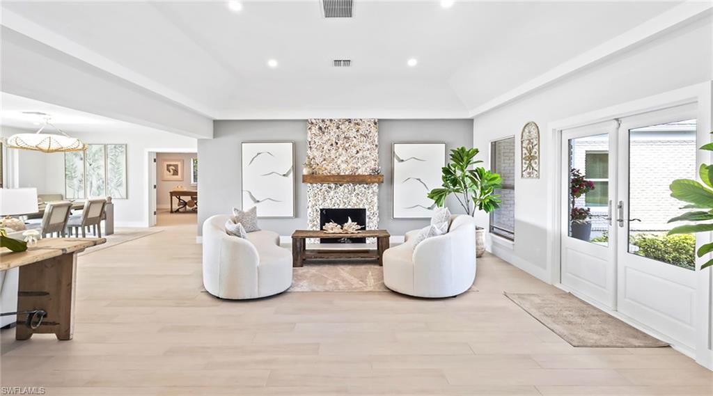 Living room with light wood-style floors, french doors, a large fireplace, a tray ceiling, and recessed lighting