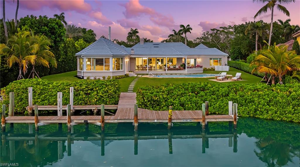 Rear view of property with a patio area, an outdoor pool, a water view, a sunroom, and a lawn