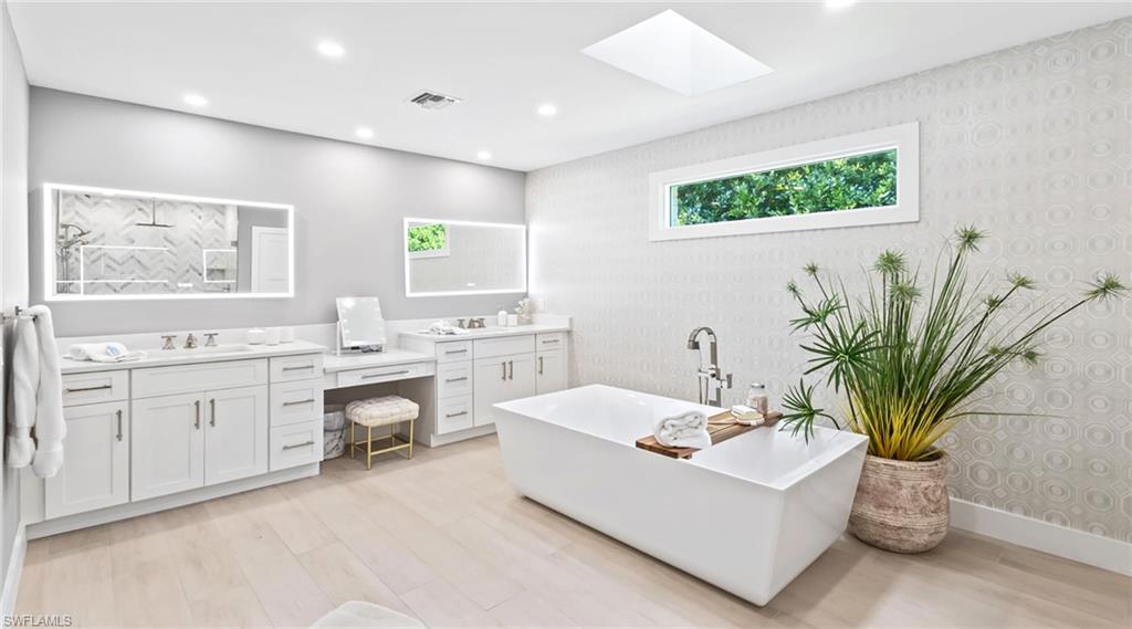 Full bath with wallpapered walls, vanity, a soaking tub, a skylight, and light wood-type flooring