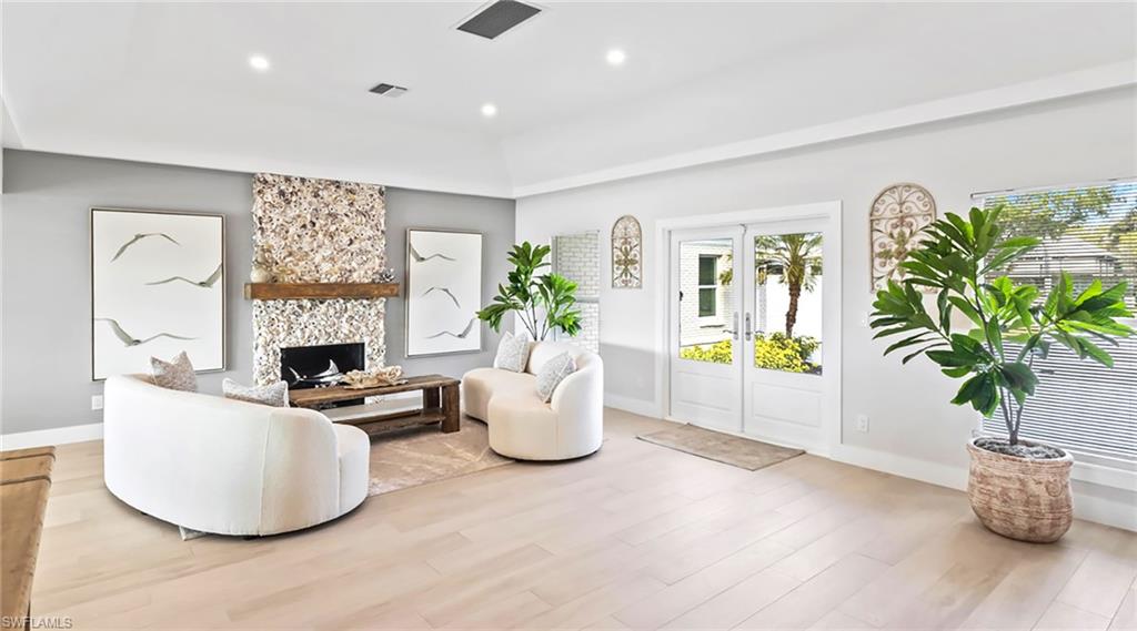 Living room with a tray ceiling, wood finished floors, recessed lighting, and a large fireplace