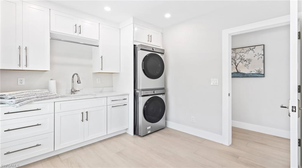 Laundry room featuring stacked washing machine and dryer, recessed lighting, light wood-type flooring, and cabinet space