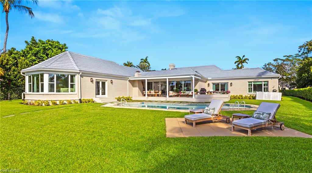 Back of house featuring a sunroom, a patio, an outdoor pool, a lawn, and a tile roof