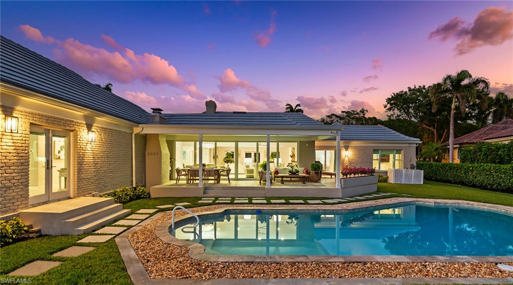 Back of house at dusk with brick siding, french doors, a chimney, a patio area, and outdoor lounge area