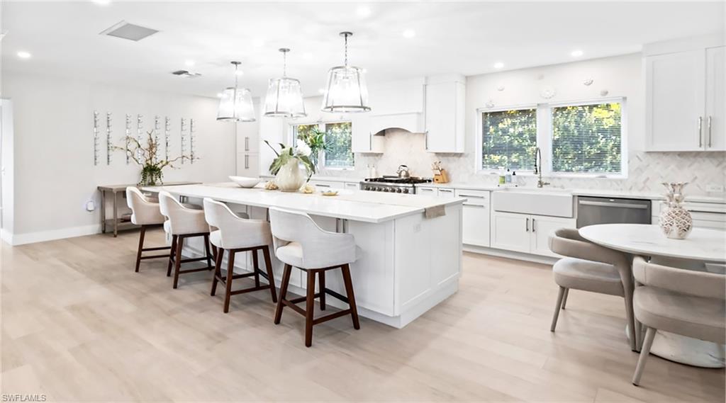 Kitchen featuring white cabinetry, a kitchen island, hanging light fixtures, a kitchen bar, and tasteful backsplash