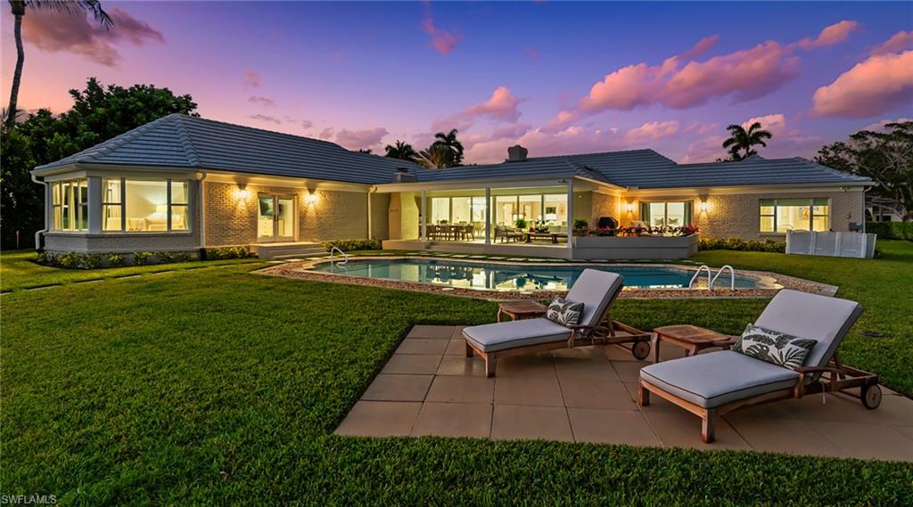 Rear view of property with a lawn, a patio, brick siding, and an outdoor pool
