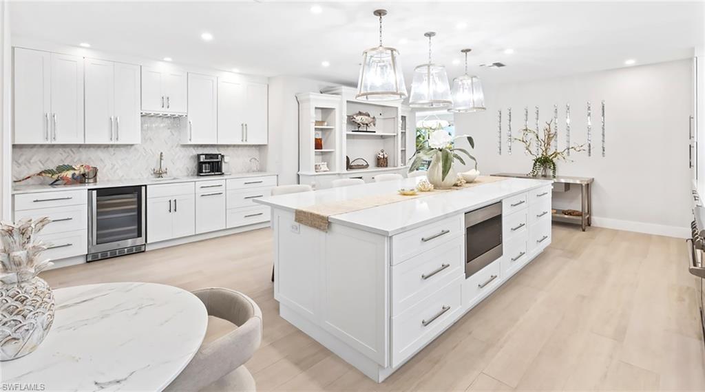 Kitchen featuring white cabinets, beverage cooler, decorative light fixtures, stainless steel microwave, and a center island